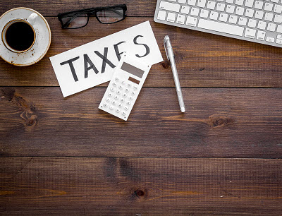 desk with note that reads taxes along with keyboard and coffee cup
